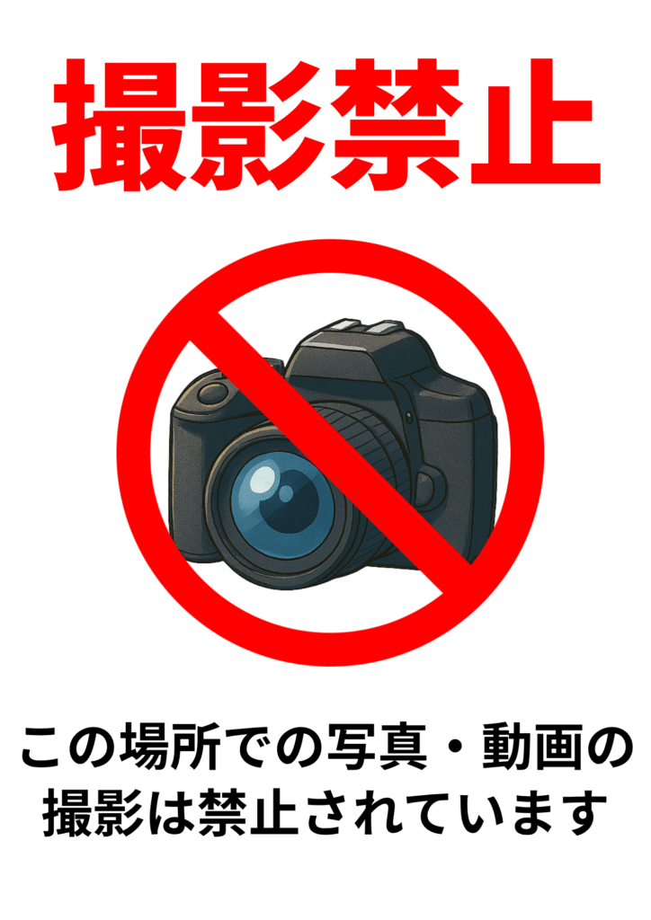 「撮影禁止」と大きく赤文字で書かれた張り紙。中央にはカメラのイラストに赤い禁止マークが重ねられており、下部には「この場所での写真・動画の撮影は禁止されています」と注意書きがある